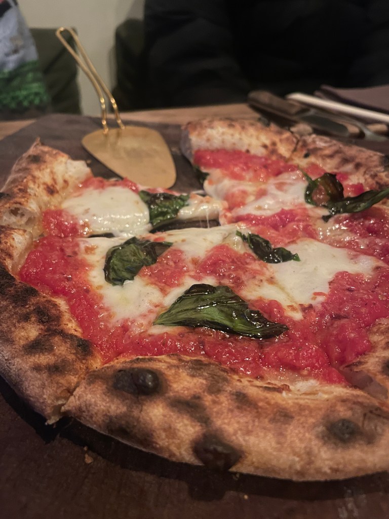 A Margherita pizza with a slice missing. A pizza slice server is also on the board.

