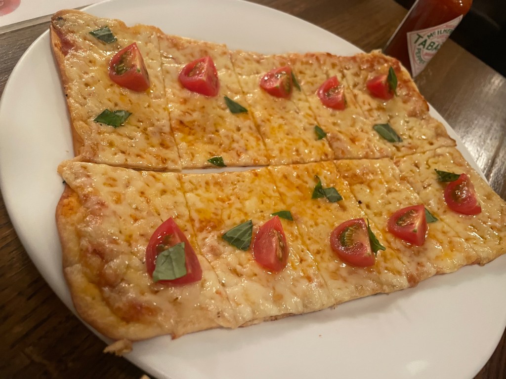 a rectangle shaped pizza on a white plate, with slices of cherry tomatoes and fresh basil on top
